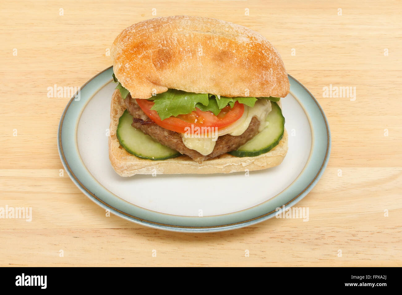 Cheeseburger con insalata in una ciabatta roll su una piastra su un tavolo in legno Foto Stock