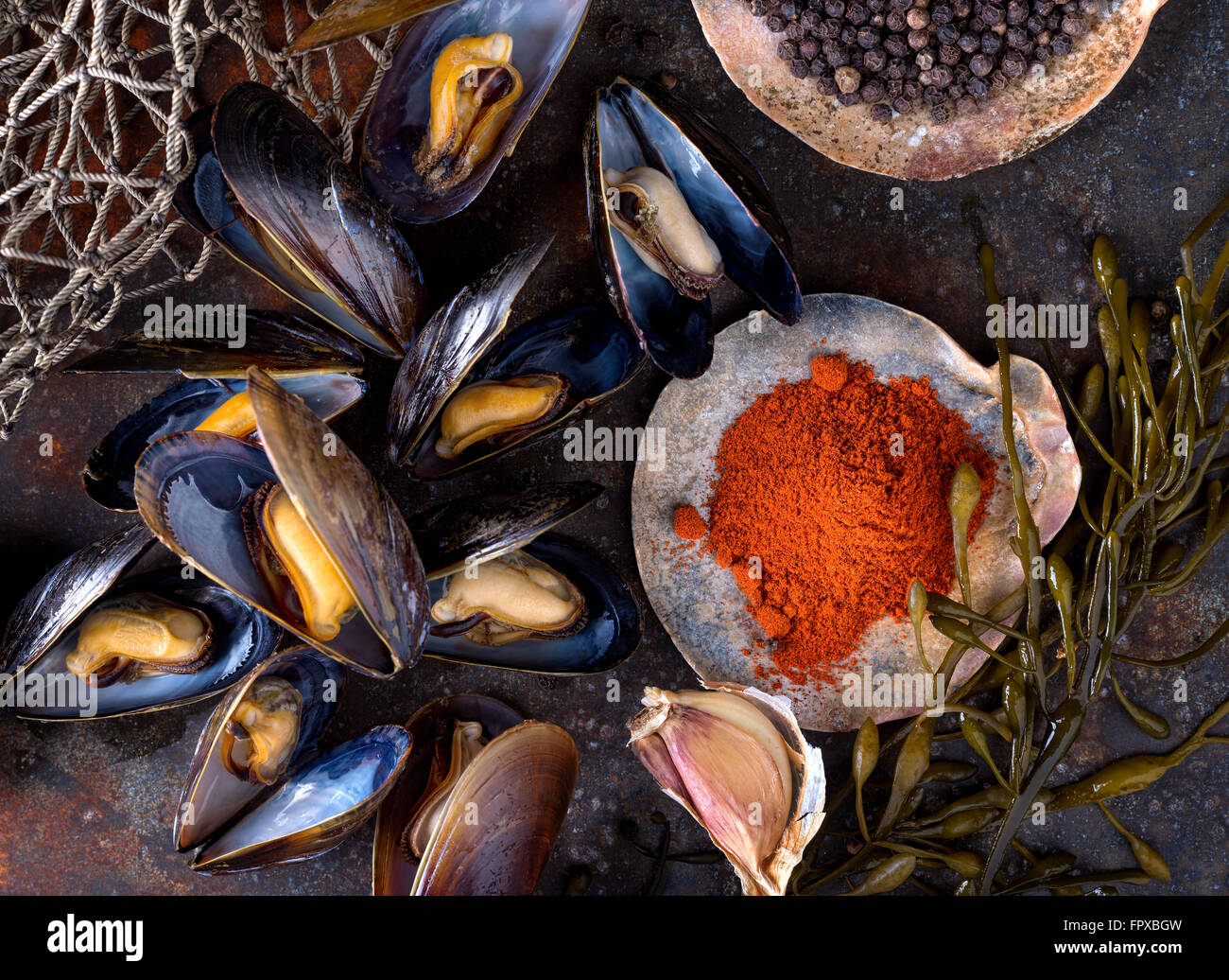 Le cozze al vapore su un sfondo rustico con peperoncino, pepe, aglio e alghe. Foto Stock