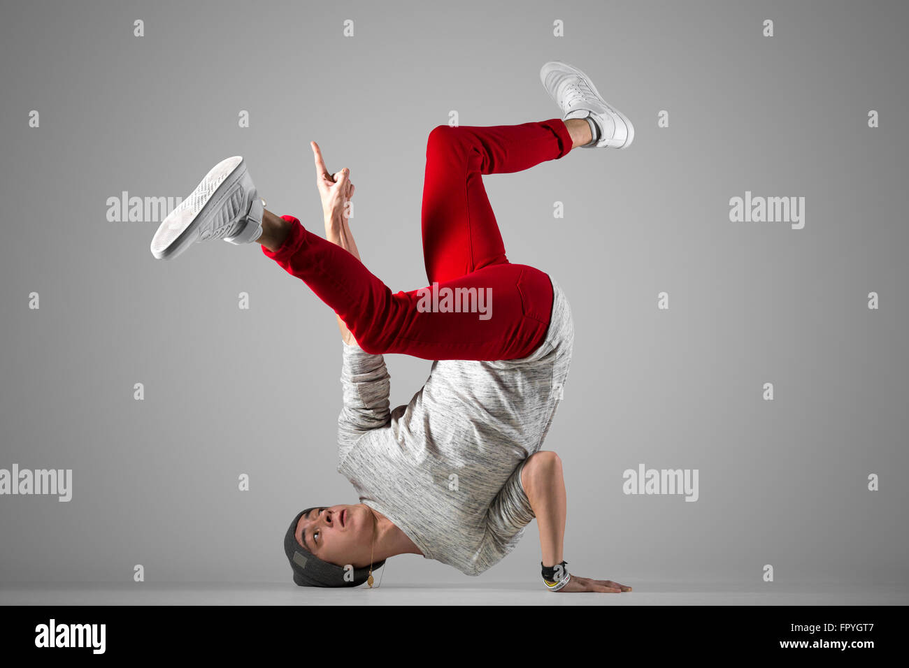 Montare un giovane uomo in rosso casual jeans, esecuzione di breakdance si muove sul pavimento. Lunghezza completa di foto su studio ba grigio Foto Stock