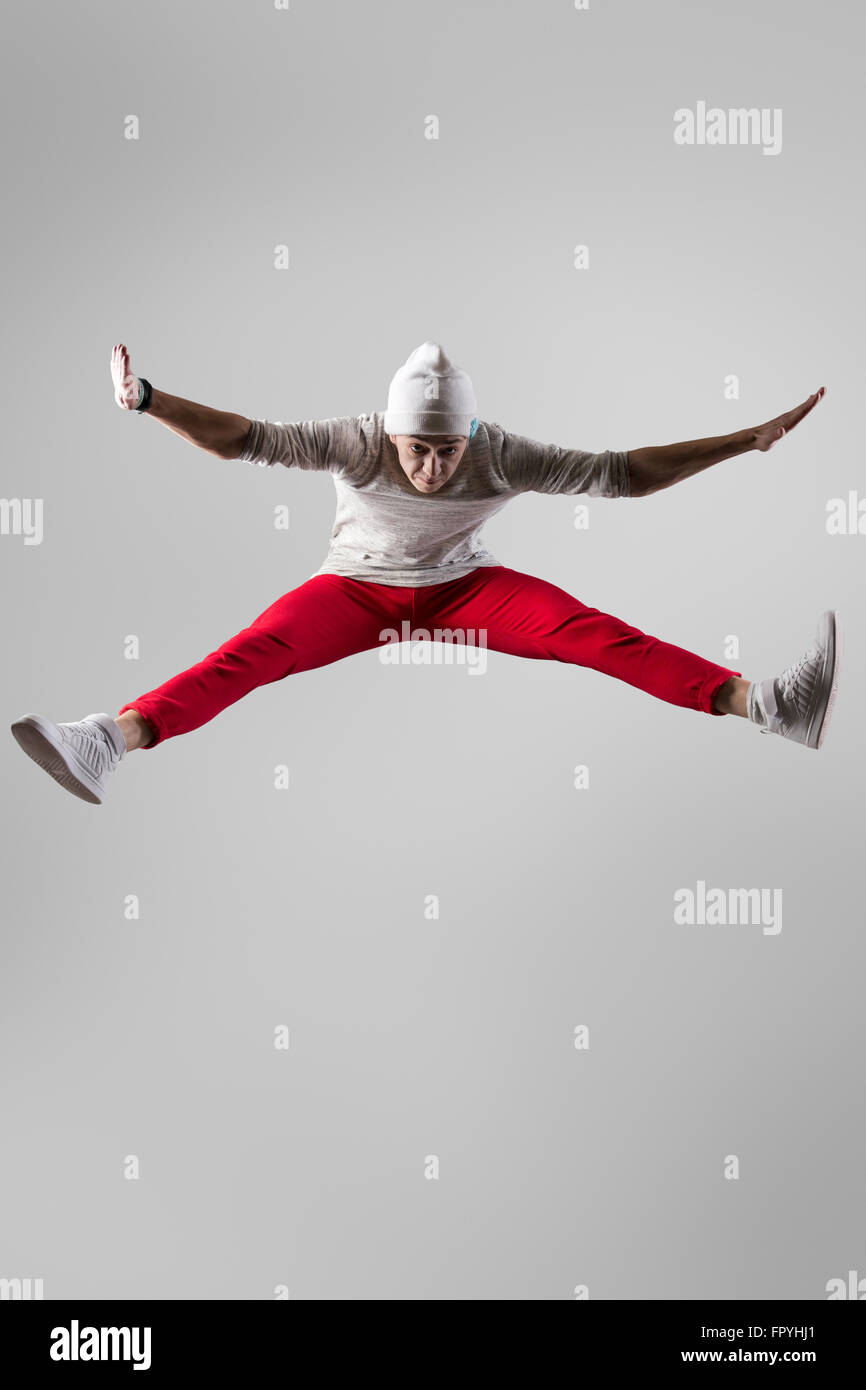 Un giovane di stile urbano guy breakdancer in casuale pantaloni rossi e beanie che lavora fuori, ballare e saltare. Lunghezza completa foto sul prigioniero Foto Stock