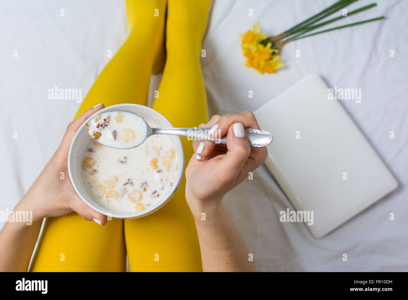 Ragazza mangiare cereali nel letto di indossare calze di colore giallo Foto Stock