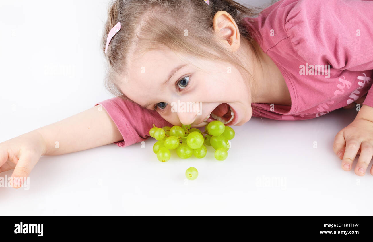 Baby girl sdraiato e mangiare uva verde. Studio shot. Foto Stock