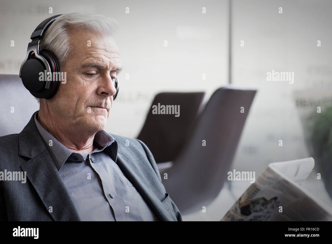 Imprenditore senior con le cuffie per ascoltare musica e leggere il giornale Foto Stock