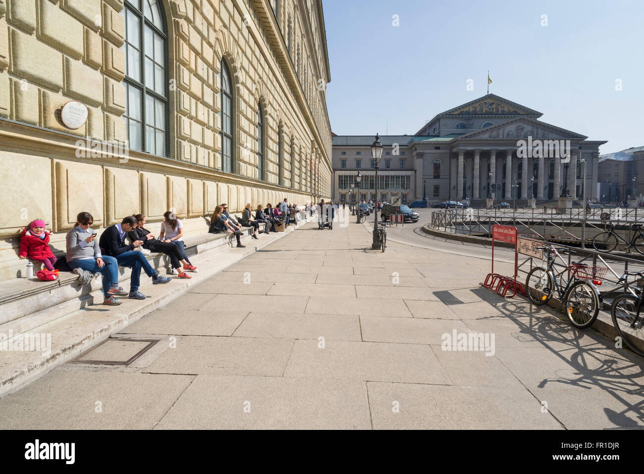 La gente seduta al royal Königsbau palace e il teatro di Monaco di Baviera godersi il caldo sole di primavera,Baviera,Germania Foto Stock