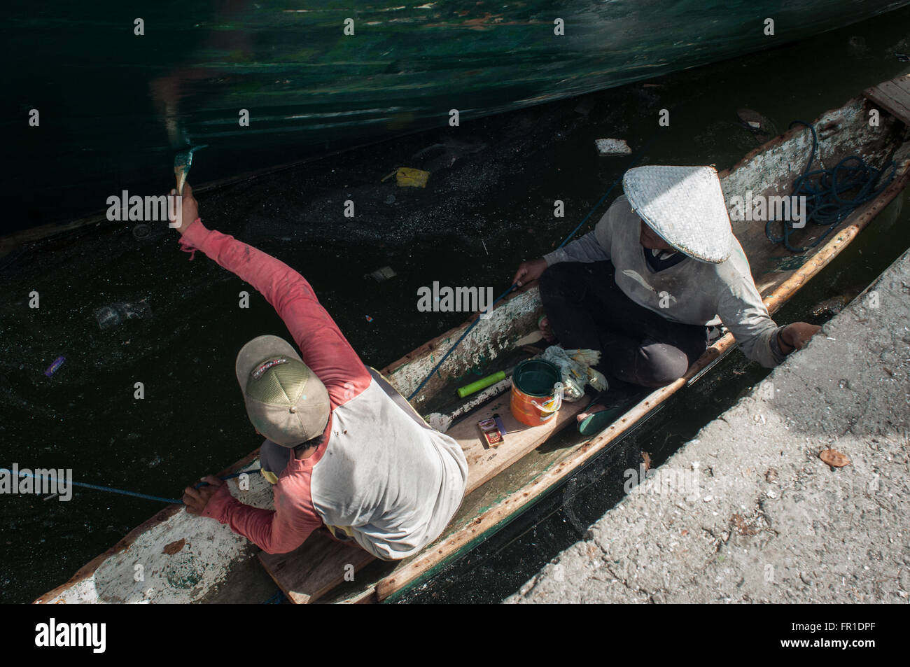 Un uomo vernici lo scafo di una barca al porto Paotere. Foto Stock