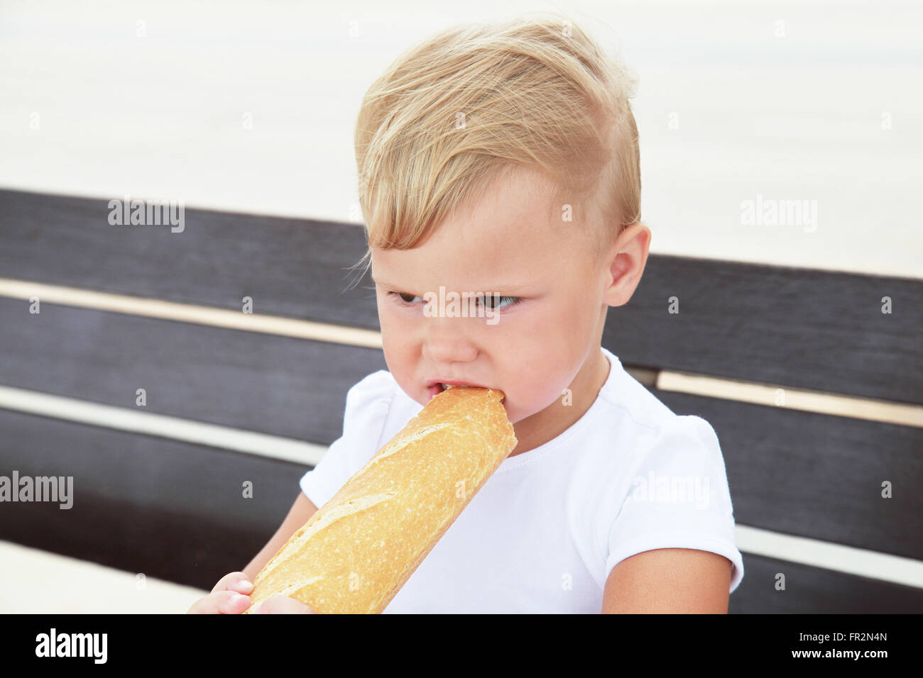 Outdoor close-up ritratto di carino bionda caucasica bambina mangiare grandi baguette francese Foto Stock