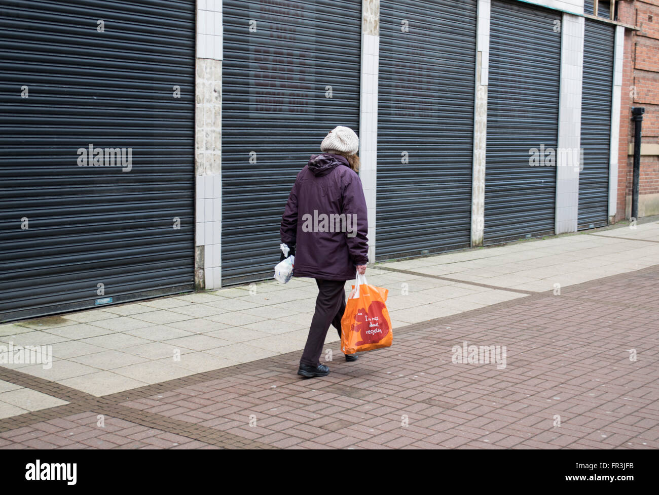Una donna a camminare lungo una fila di chiusura negozi in Stretford, Manchester, Inghilterra, Regno Unito Foto Stock