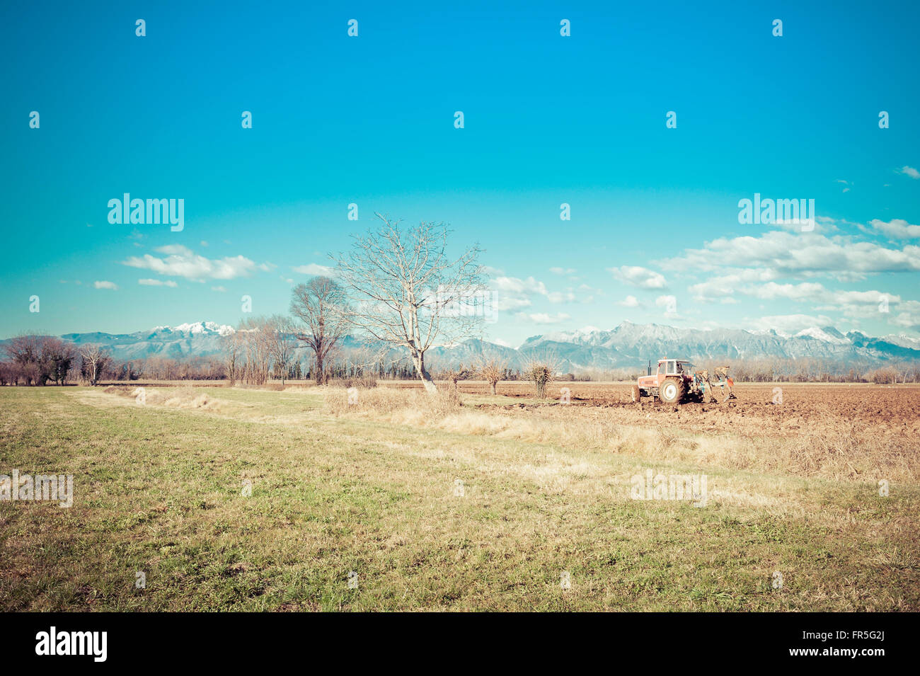 Il paesaggio agricolo. Con il trattore arare un campo. Le montagne sullo sfondo. Foto Stock