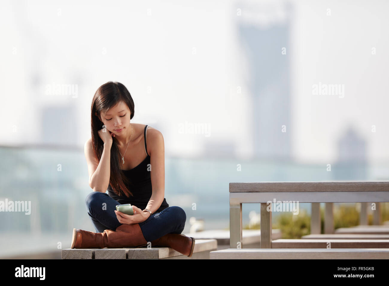 Donna texting sul banco di prova all'aperto Foto Stock