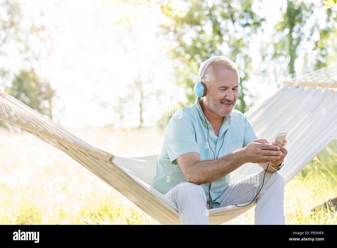 Senior uomo con le cuffie per ascoltare musica con il lettore mp3 in estate amaca Foto Stock