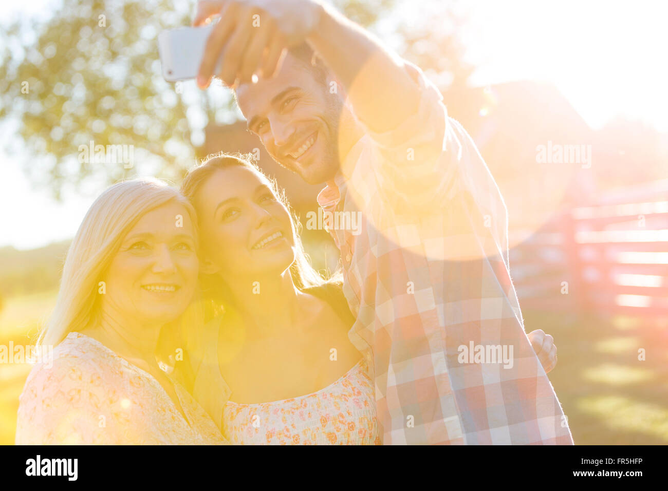 Madre e figli adulti tenendo selfie nel cortile soleggiato Foto Stock