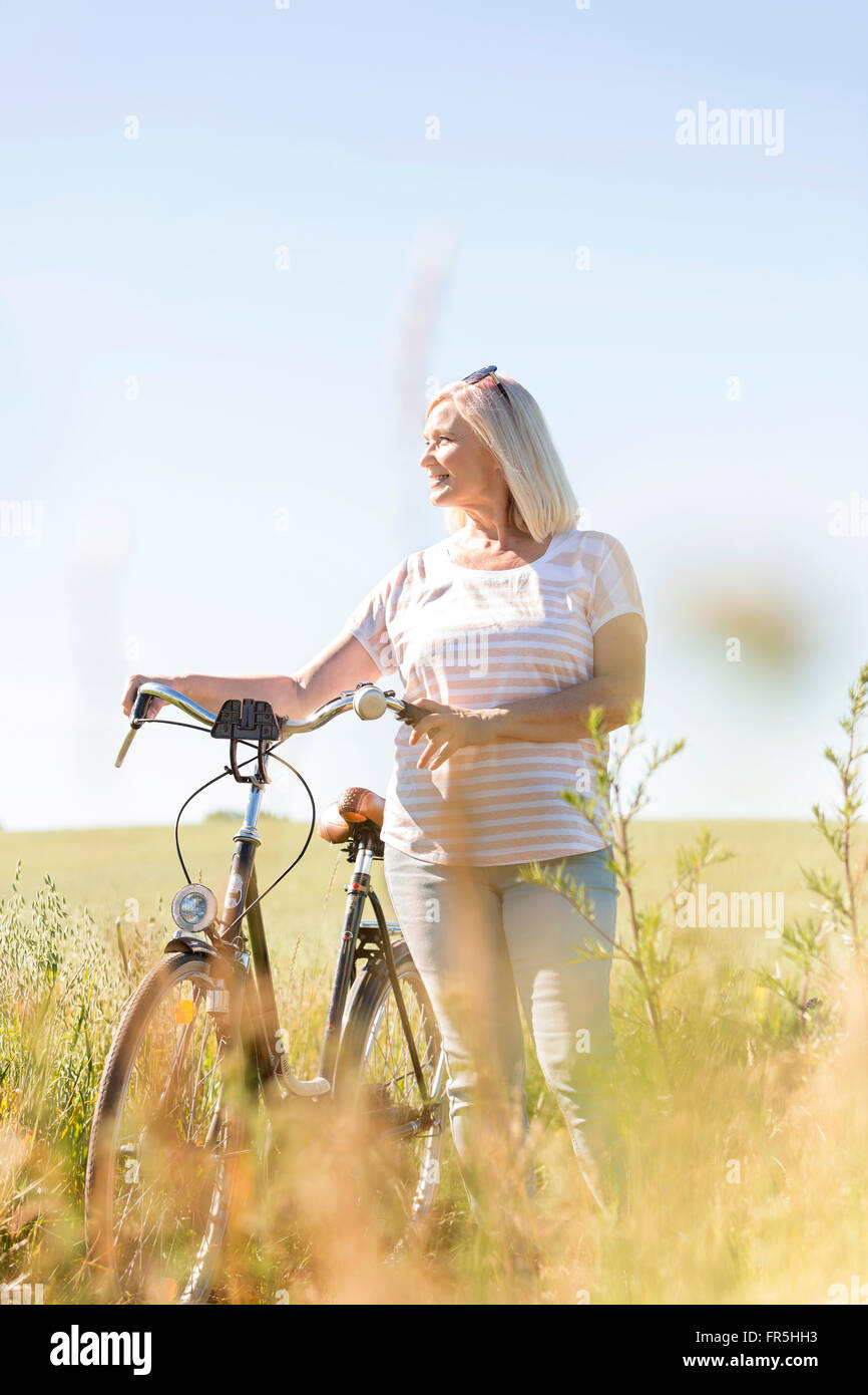 Senior donna con la bicicletta alla ricerca di distanza nel campo di sole Foto Stock