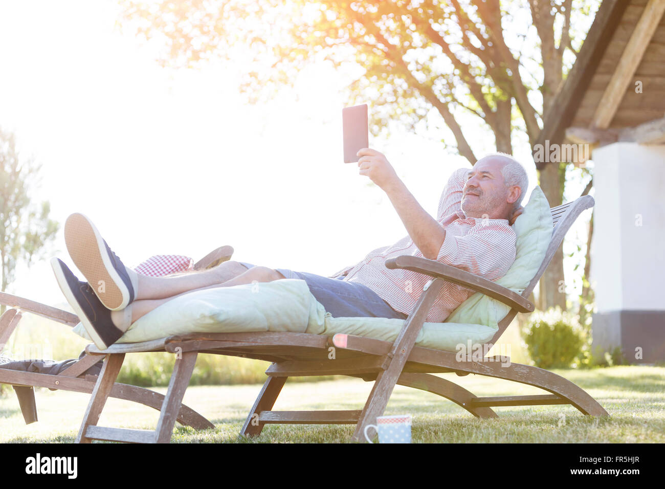 Senior uomo con tavoletta digitale su rilassante lounge chair in cortile Foto Stock