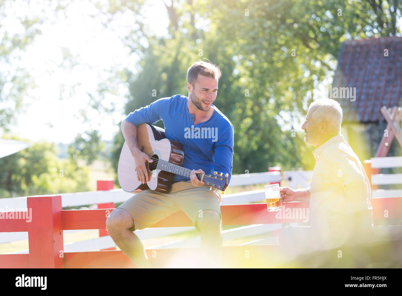 Padre di bere birra e ascolto di figlio adulto a suonare la chitarra Foto Stock