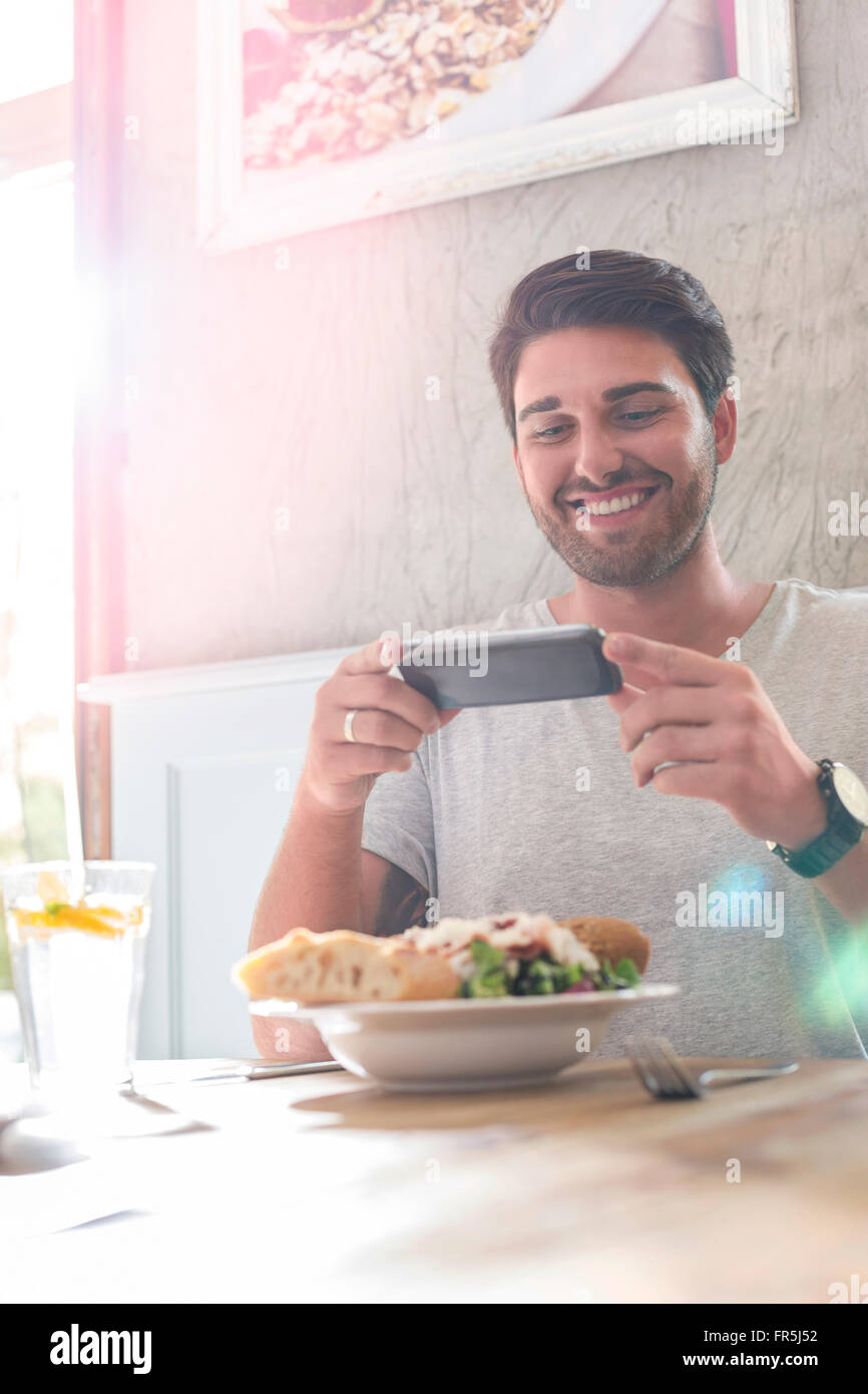 Uomo sorridente a fotografare il pranzo al cafè tabella Foto Stock