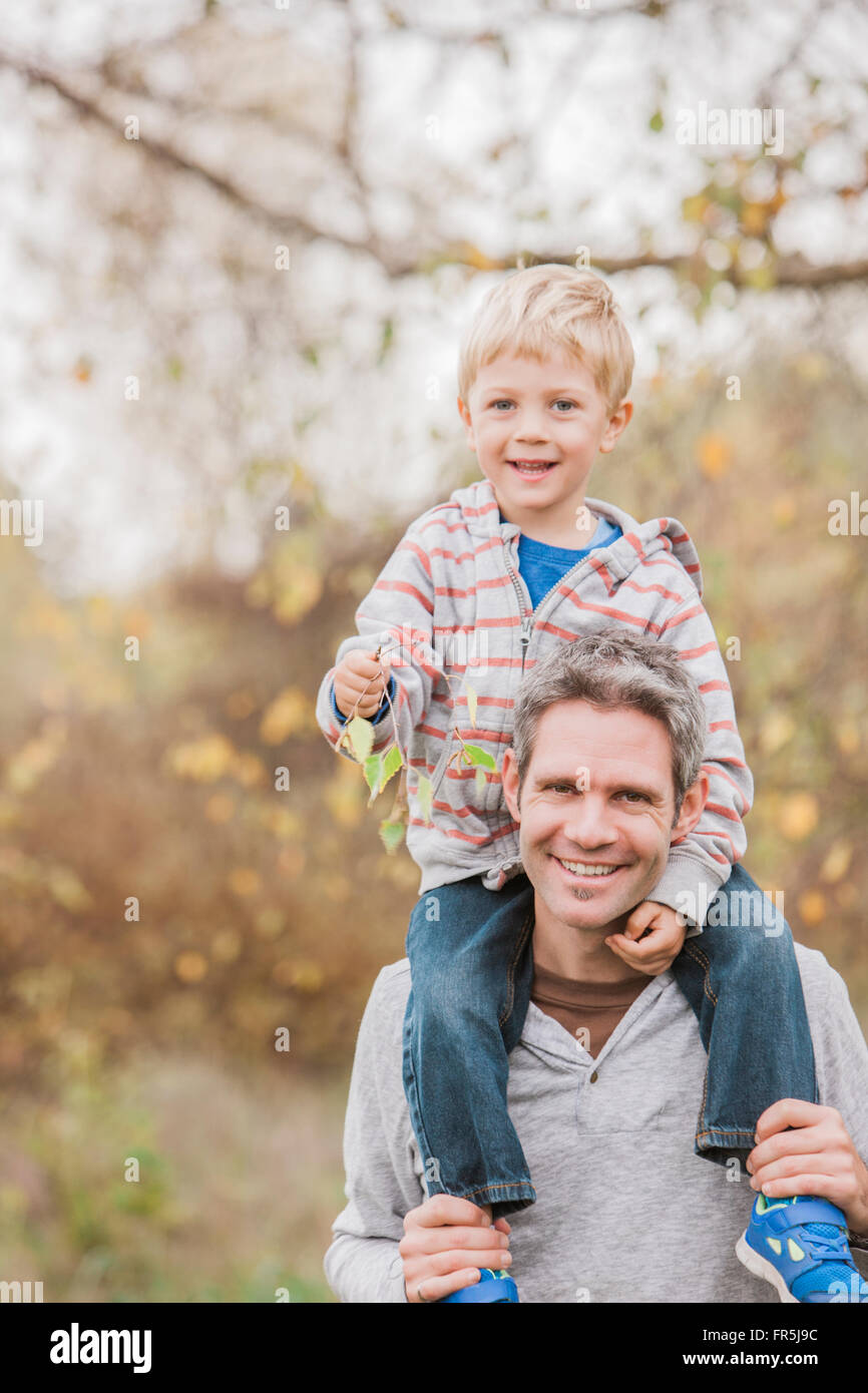 Ritratto di Padre sorridente che trasportano il toddler figlio sulle spalle in autunno park Foto Stock