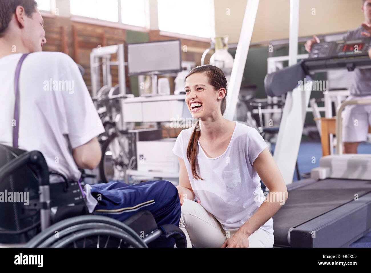 Sorridente terapista fisico parlando di uomo in sedia a rotelle Foto Stock