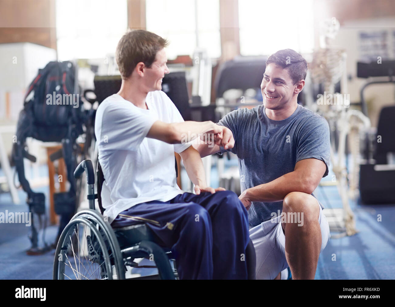 Fisioterapista fist bumping uomo in sedia a rotelle Foto Stock