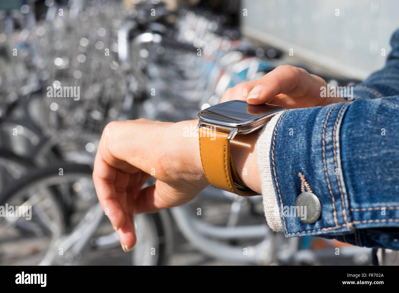 Donna in città con applicazione su smartwatch. Fila di biciclette a noleggio, sfondo Foto Stock