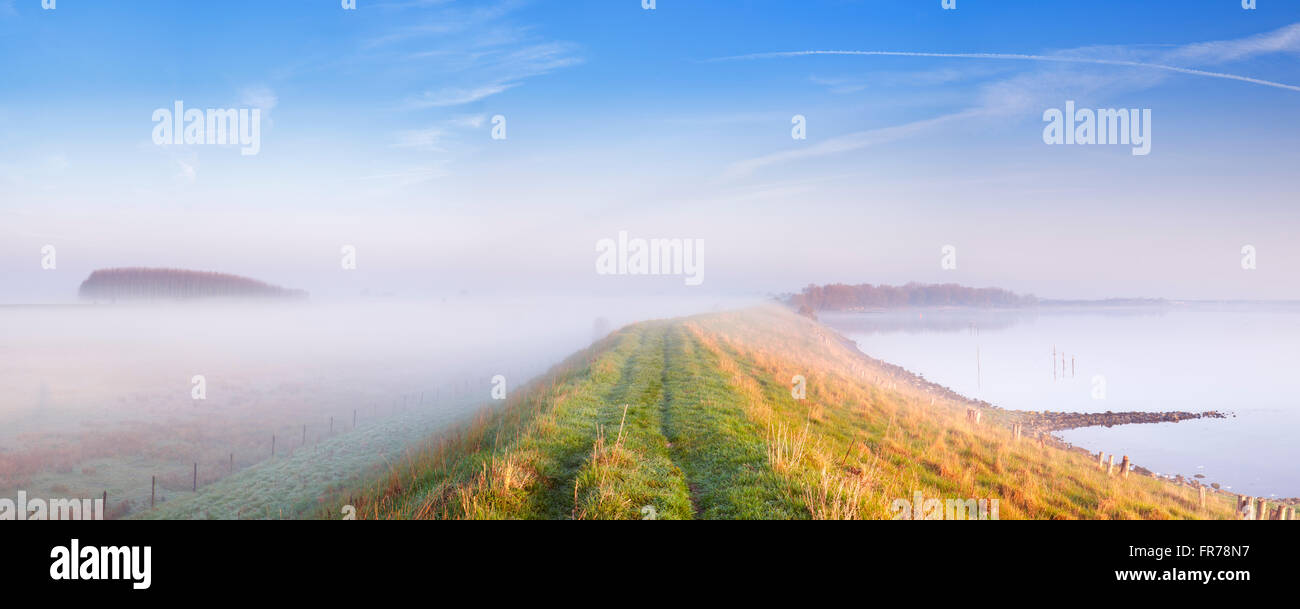 Un tipico paesaggio dei polder Olandesi con una diga lungo un lago. Fotografato alla Veerse Meer nella provincia di Zelanda su una nebbia Foto Stock