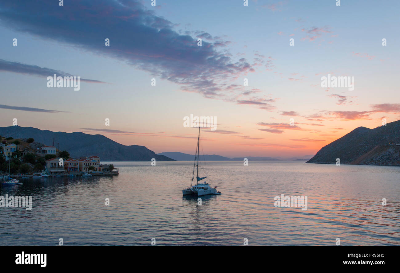 Gialos, Symi, Egeo Meridionale, Grecia. Vista su tutta la baia Harani all'alba, catamarano al di ancoraggio. Foto Stock