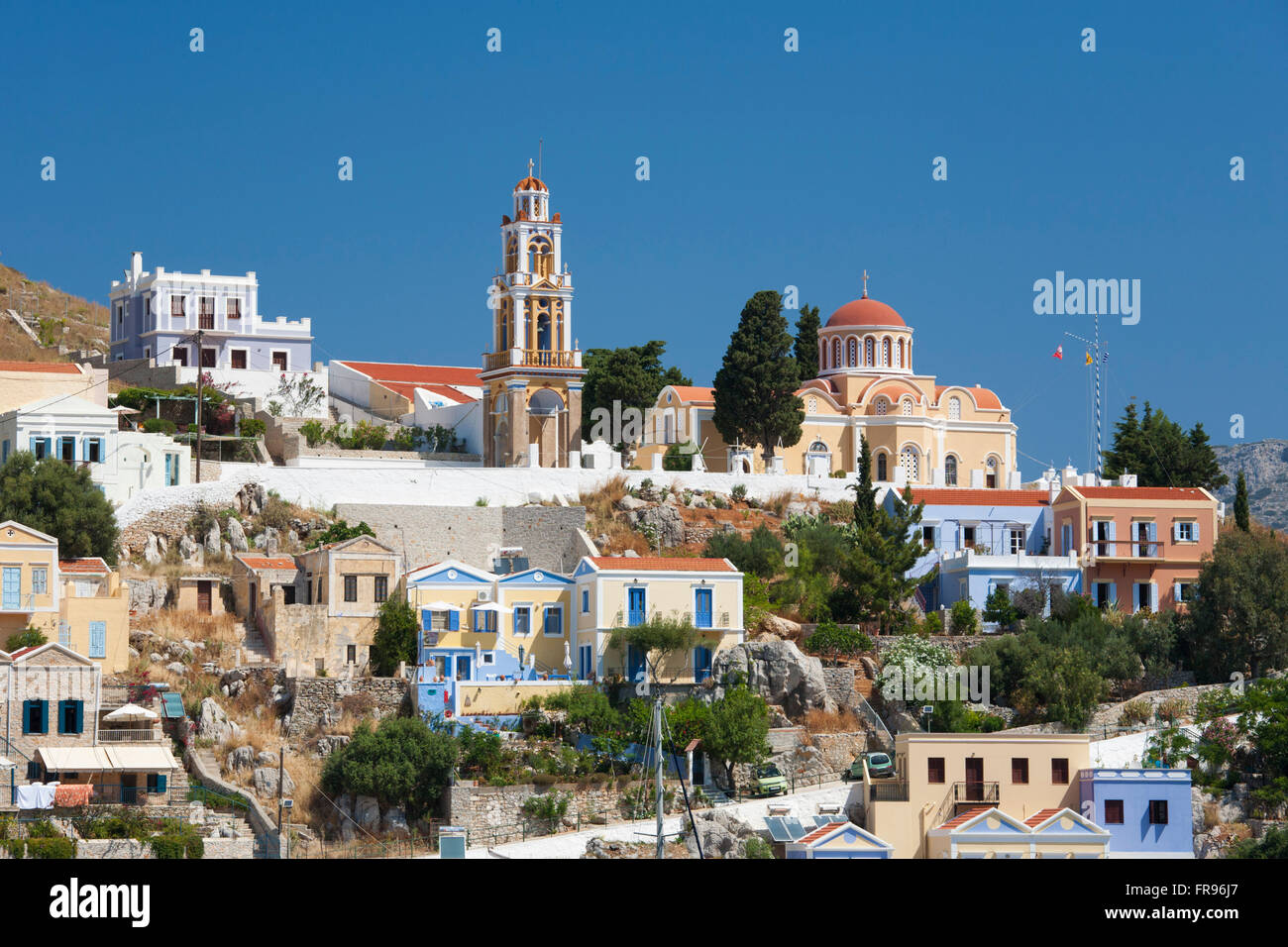 Gialos, Symi, Egeo Meridionale, Grecia. Hilltop chiesa e case colorate sopra Harani Bay. Foto Stock