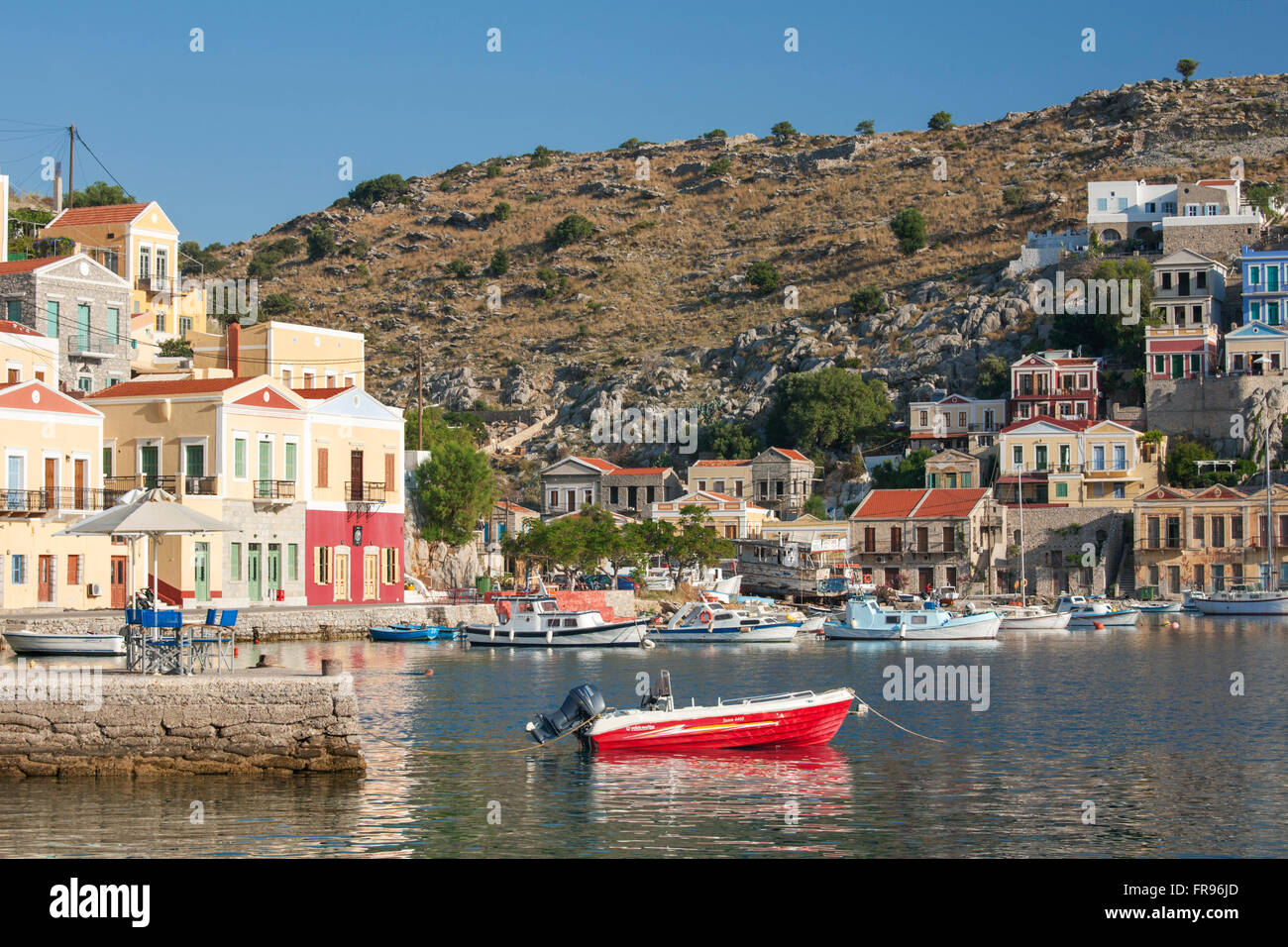 Gialos, Symi, Egeo Meridionale, Grecia. Vista su tutta la baia Harani, colorato di barca in primo piano. Foto Stock