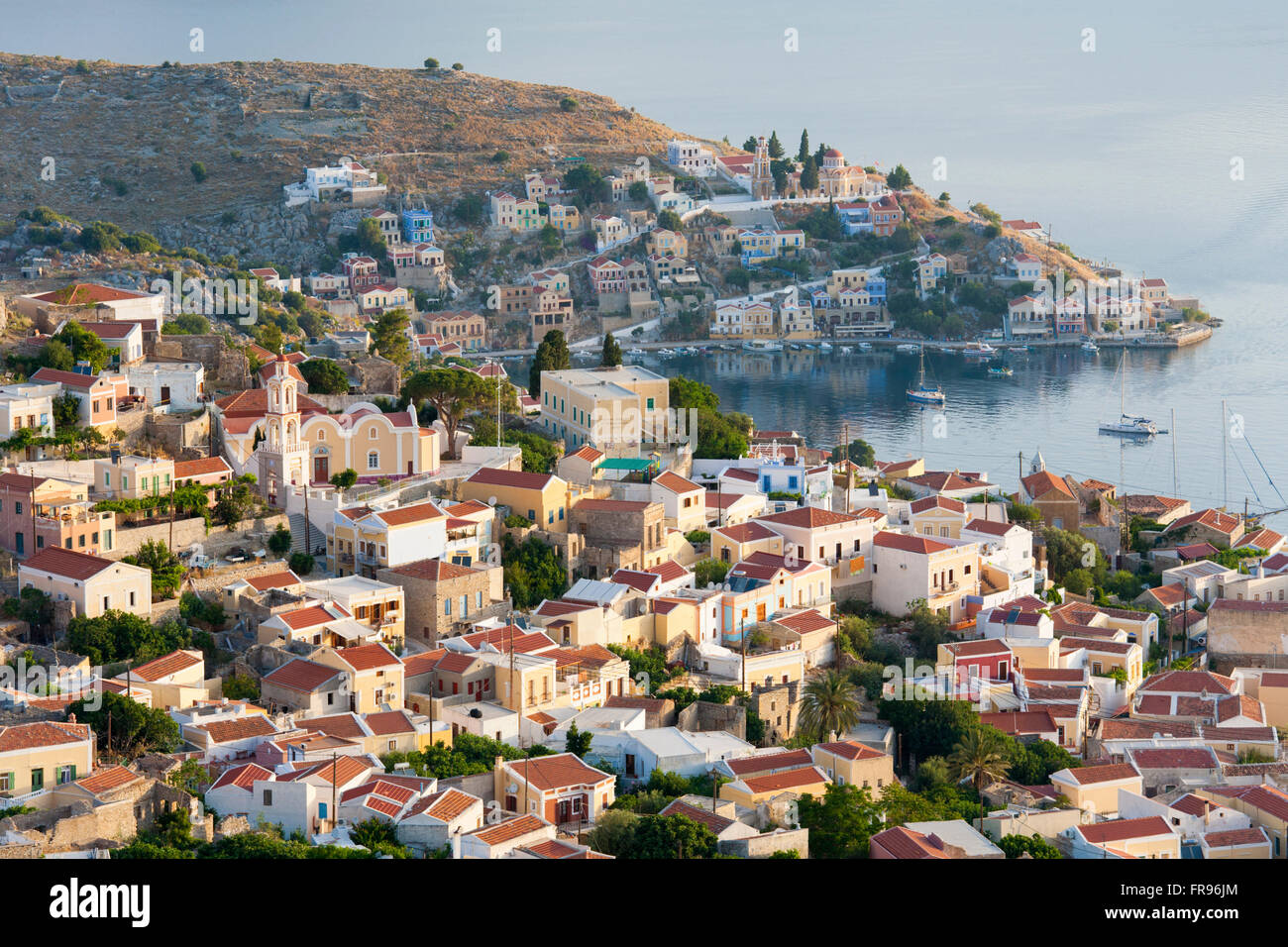 Horio, Symi, Egeo Meridionale, Grecia. Vista sui tetti di villaggio distante Harani Bay. Foto Stock