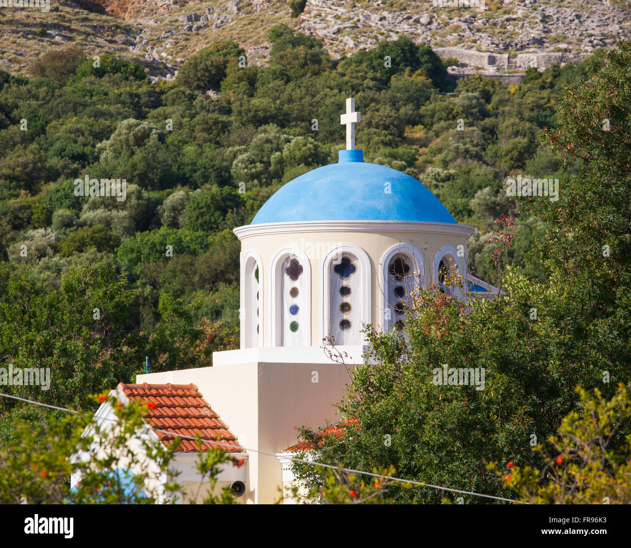 Pazienti pediatrici, Symi, Egeo Meridionale, Grecia. Tipico blu-cupola chiesa al di sotto della collina boscosa. Foto Stock