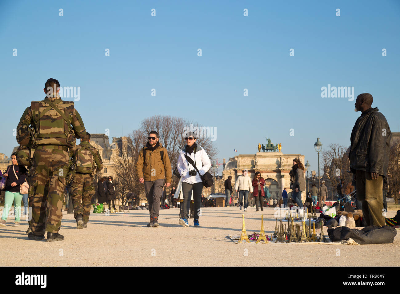 Migrante africano che vende souvenir nel Jardin des Tuileries a Parigi, in Francia in inverno sotto la sorveglianza dei soldati francesi Foto Stock