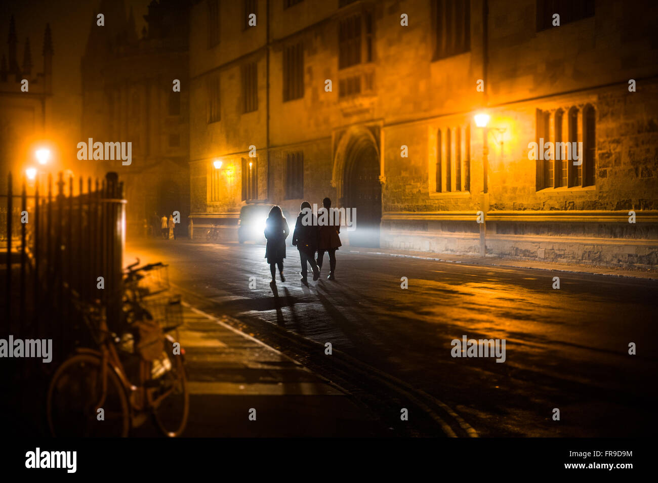 Tre stagliano gli studenti a piedi passato biblioteca Bodleian Library nella notte tempo verso Radcliffe Camera in Oxford, Regno Unito Foto Stock