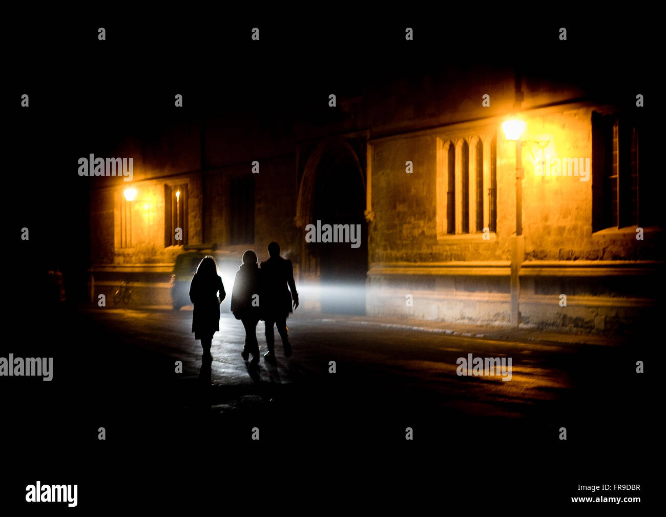 Tre stagliano gli studenti a piedi passato biblioteca Bodleian Library nella notte tempo verso Radcliffe Camera in Oxford, Regno Unito Foto Stock