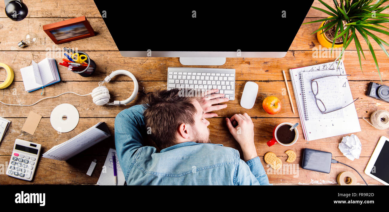 Imprenditore dormire sulla scrivania, ufficio gadget e materiali di consumo Foto Stock