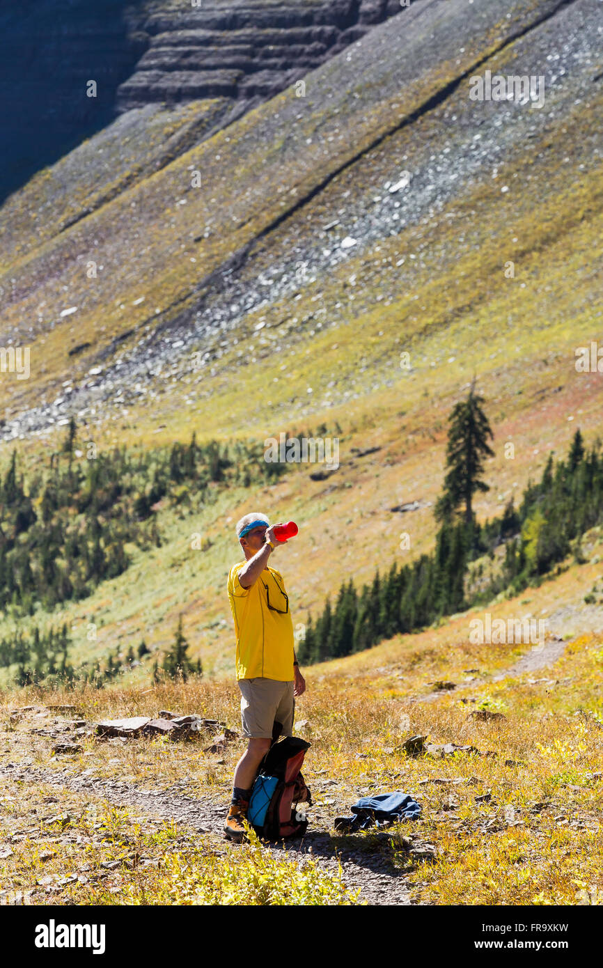 Escursionista maschio sul sentiero prendendo un drink di acqua dal flacone con pendenza lato montagna in background; Waterton, AB, CA Foto Stock