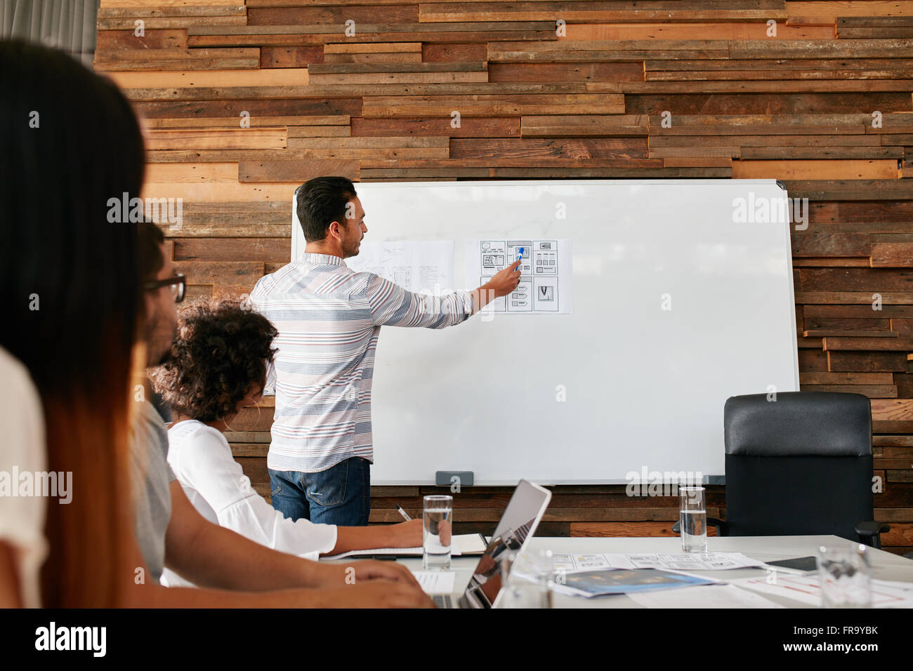 Il brainstorming in una sala riunioni di agenzia creativa. Un gruppo di giovani adulti seduti a tavola con l uomo che mostra la nuova mobile appl Foto Stock