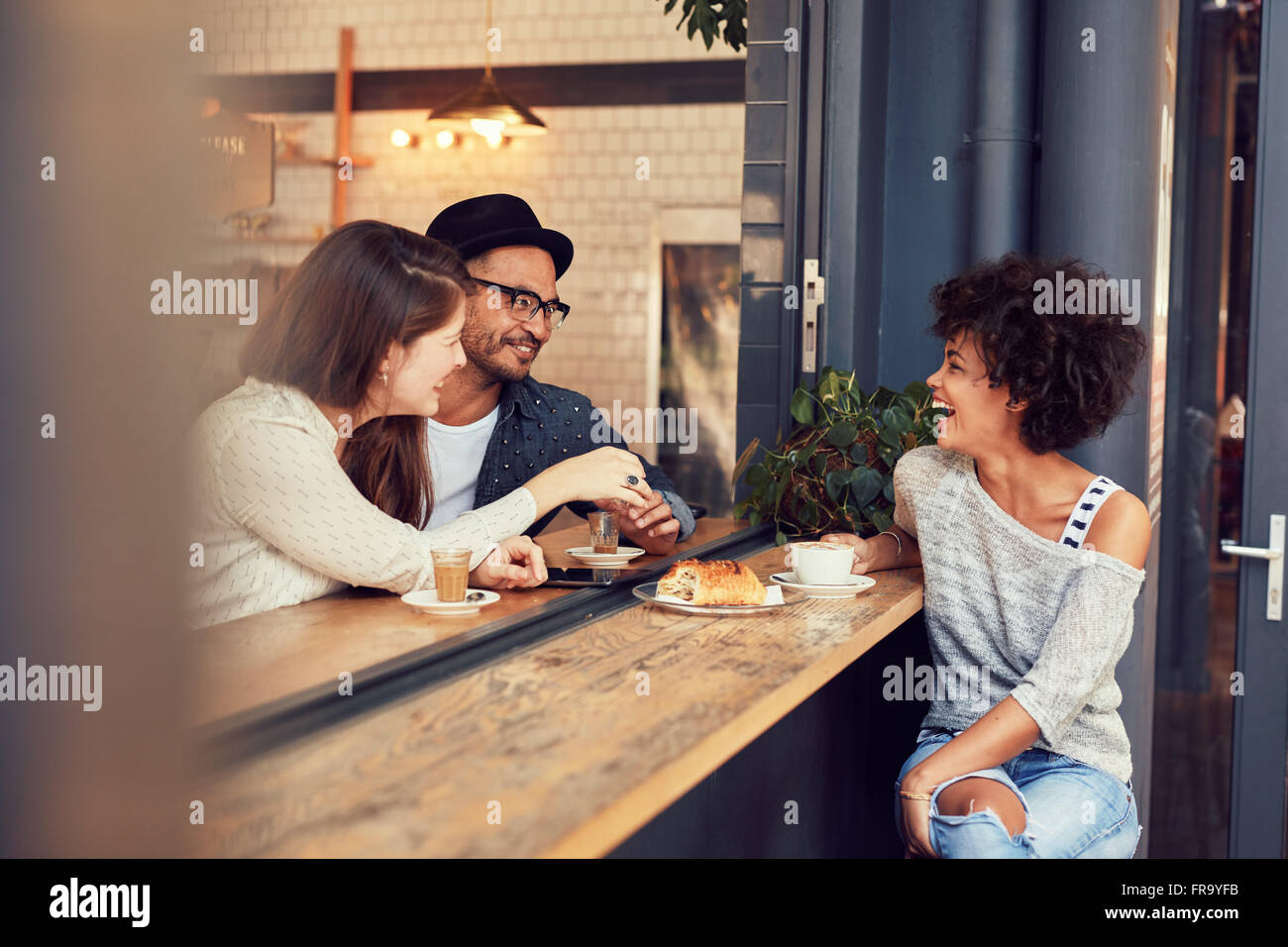 Ritratto di felice giovani seduti insieme ad un cafe avente un po' di cibo e caffè. Gruppo di amici riuniti in un coffee shop Foto Stock