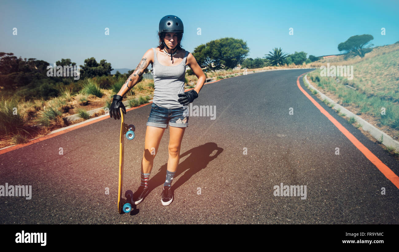 A piena lunghezza Ritratto di giovane donna in piedi su una strada di campagna con un longboard. Foto Stock