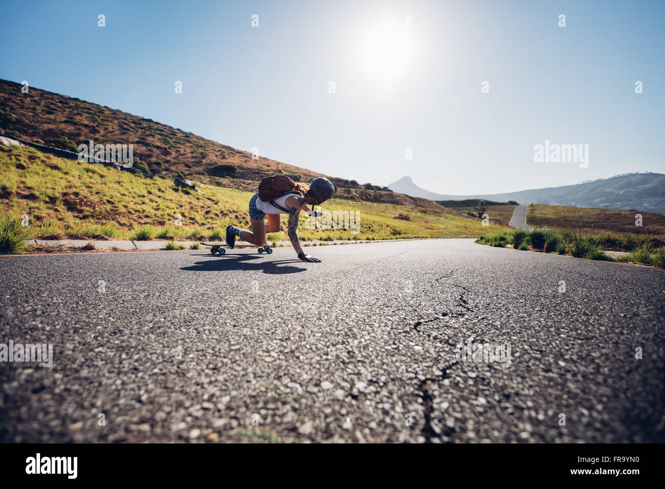 Vista posteriore del giovane pattinatore femmina praticare lo skateboard su strade rurali in una giornata di sole. Lei sta facendo acrobazie e toccando il ro Foto Stock