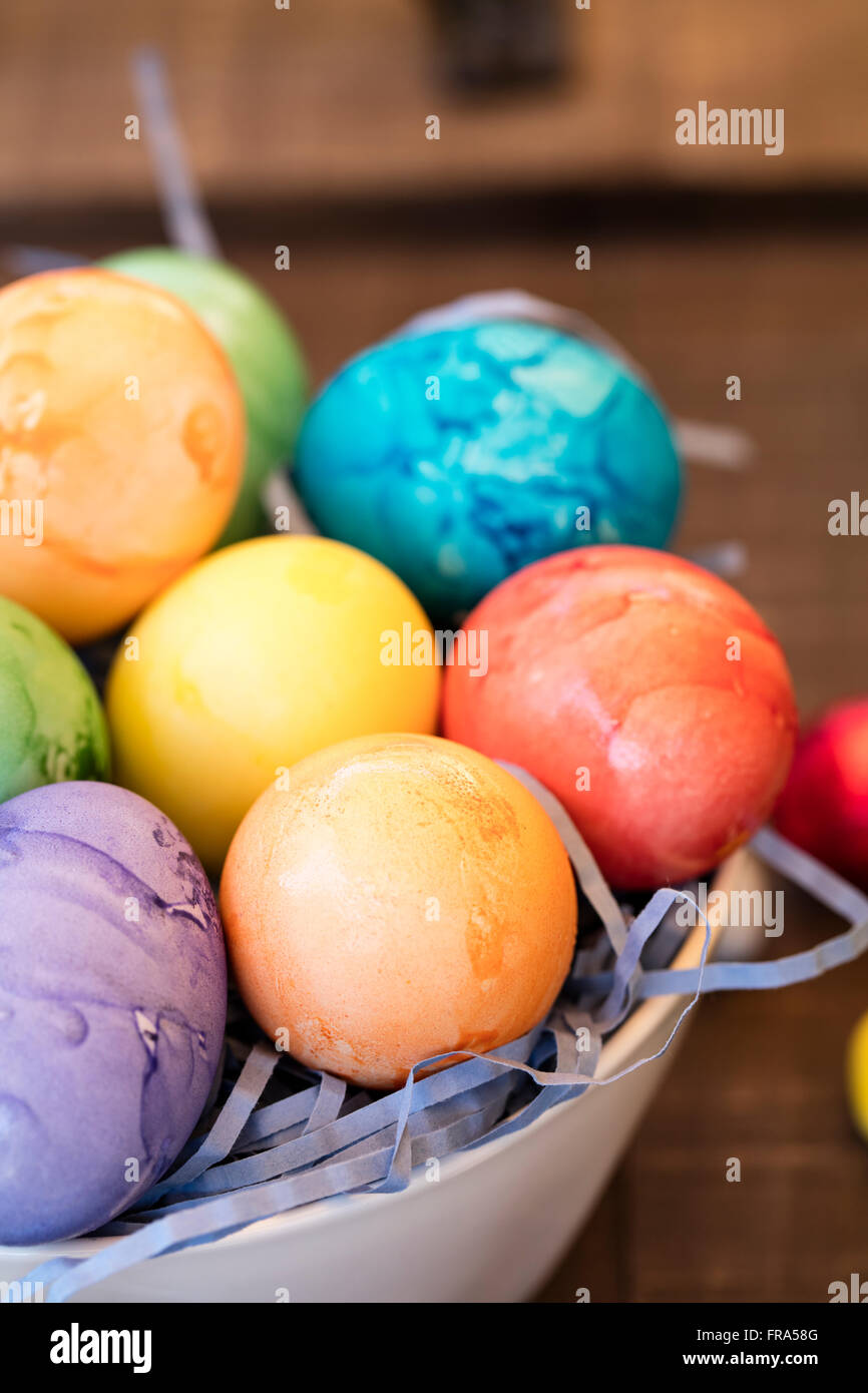 Colorate di arancione, viola, giallo, rosso e avidità di uova di pasqua in una ciotola con la caramella sulla parte superiore della tavola Foto Stock