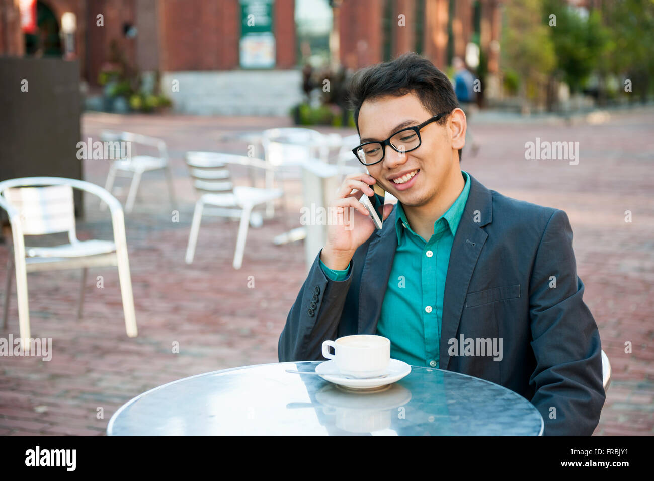Successo giovane uomo asiatico in business abbigliamento casual seduto e sorridente in un rilassante outdoor cafe con tazza di caffè a parlare su Foto Stock