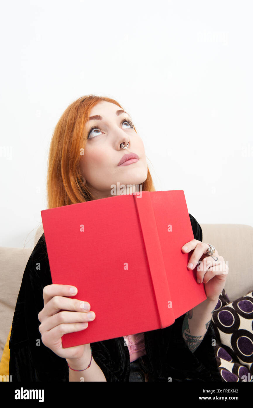 Giovane donna redhead a casa con un libro cercando Foto Stock