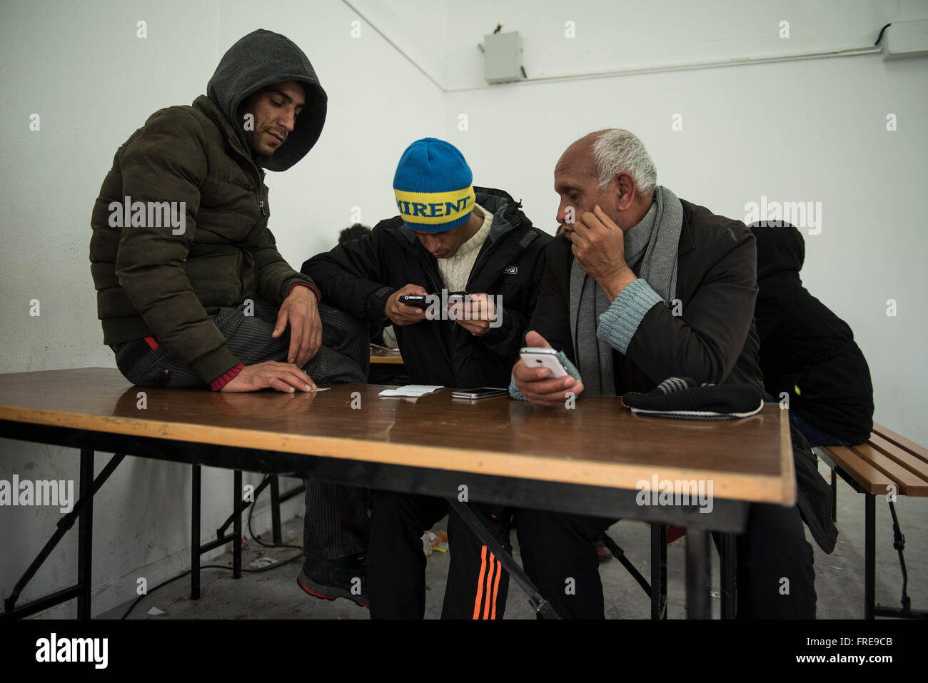 Un migrante controlla il suo cellulare come gli altri stanno a guardare, a Diavata Refugee Camp vicino al nord della città greca di Salonicco Foto Stock