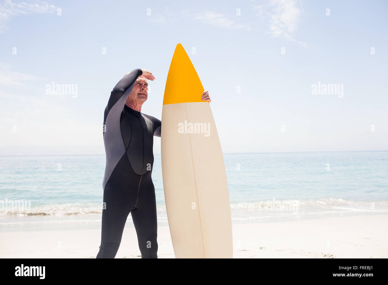 Senior uomo con tavola da surf schermare gli occhi in spiaggia Foto Stock