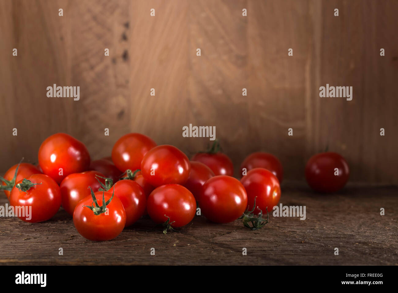 Rossi pomodori ciliegini giacente su una superficie strutturata in legno rustico sfondo con spazio di copia Foto Stock