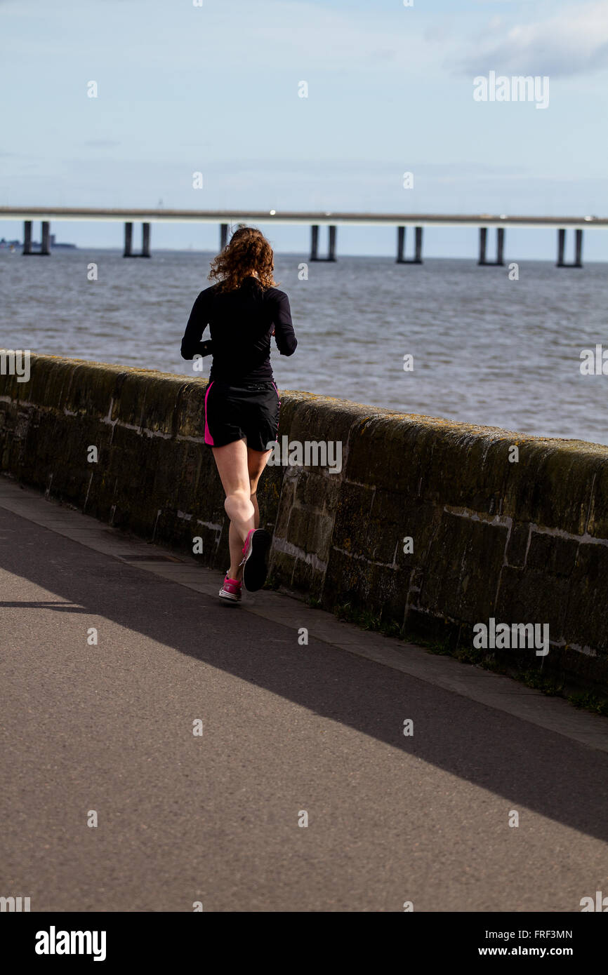 Donna jogging lungo la passeggiata lungo il fiume su un caldo sole di mattina di primavera a Dundee, Regno Unito Foto Stock