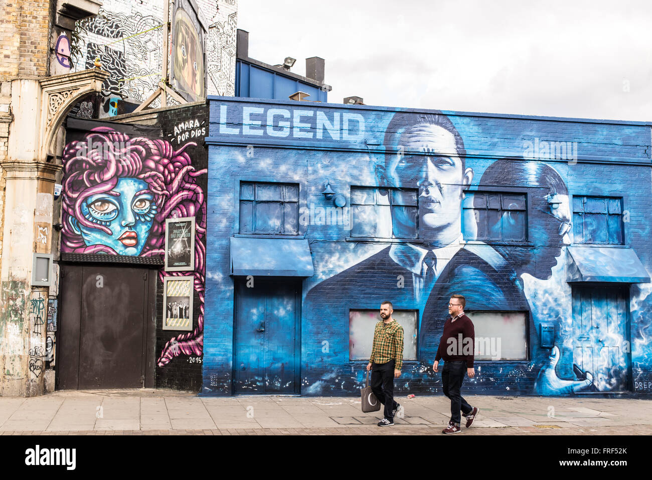 Due uomini di mezza età in piedi davanti un pezzo di strada graffiti promuovendo il rilascio della Krays' Legenda. Foto Stock