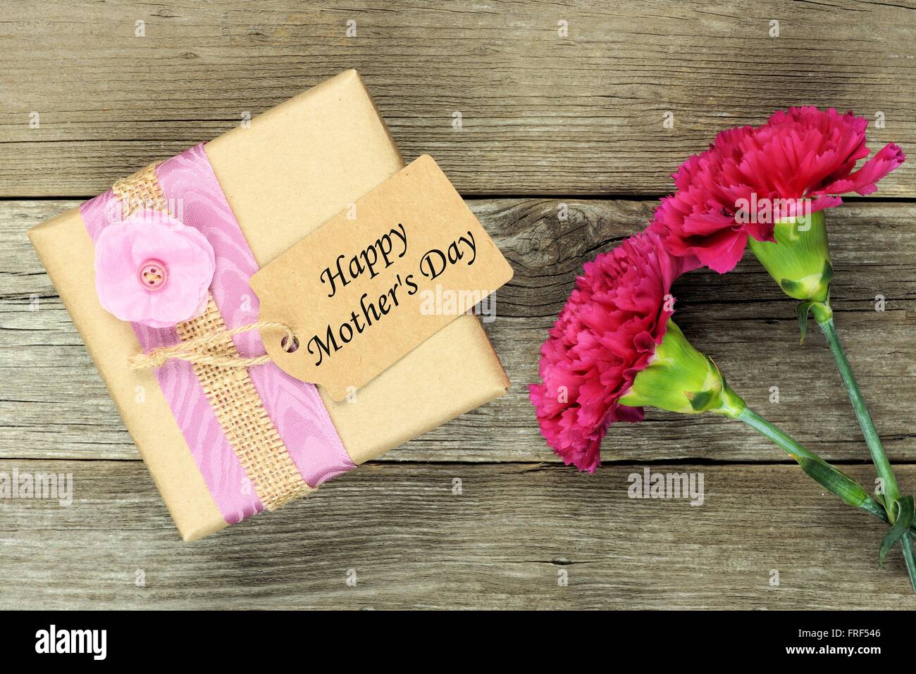 Confezione regalo con Felice Festa della Mamma tag e garofani contro un rustico sfondo legno Foto Stock