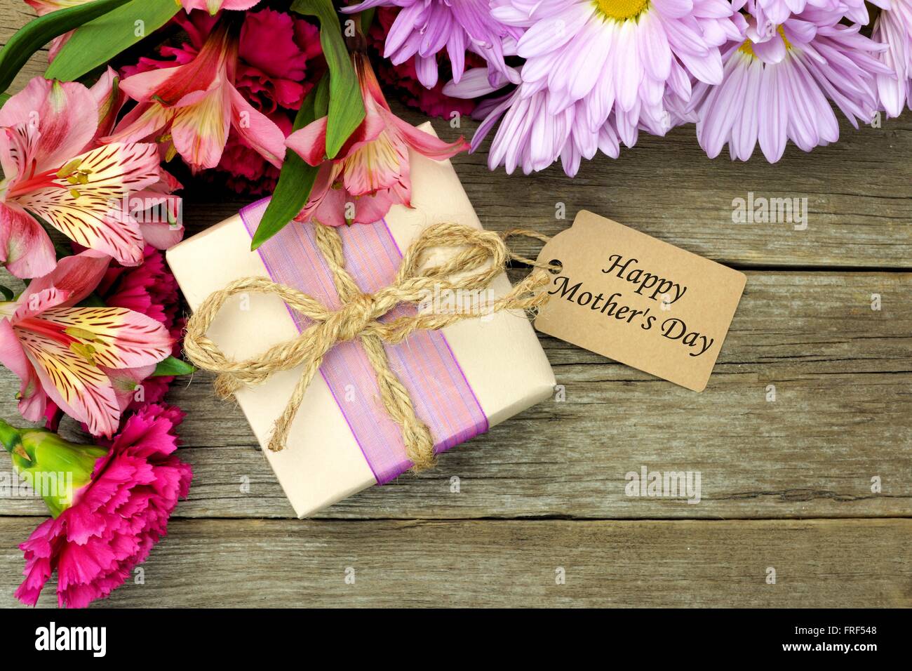 Confine di fiori con confezione regalo e una felice Festa della Mamma tag contro un rustico sfondo legno Foto Stock
