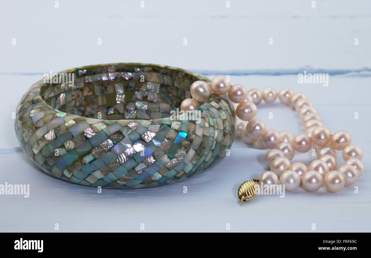 Foto di blu in legno dipinto con sfondo rosa collana di perle e blu mozaic madre perla bracciale Foto Stock