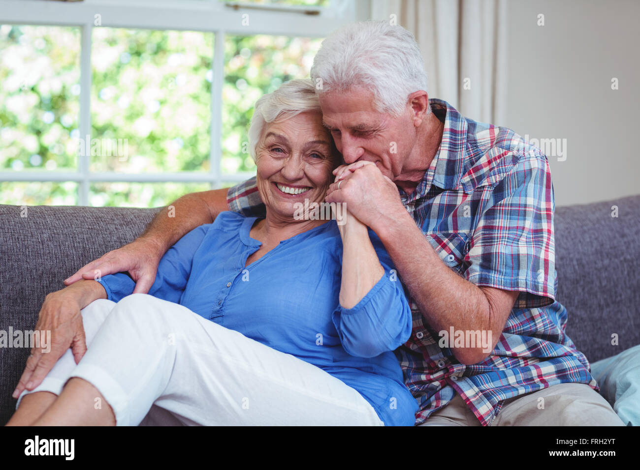 Amare senior kissing man mano moglie seduta sul divano Foto Stock